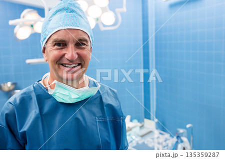 Senior male surgeon standing in OR wearing blue scrubs, cap under overhead lights, copy space Senior male surgeon standing in OR wearing blue scrubs, cap under overhead lights, copy space 135359287