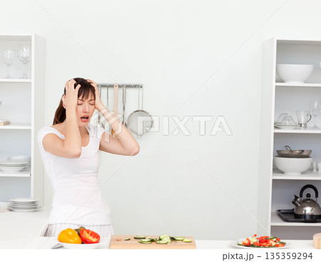 Woman pressing temples at kitchen counter with board holding sliced cucumbers, peppers, copy space 135359294