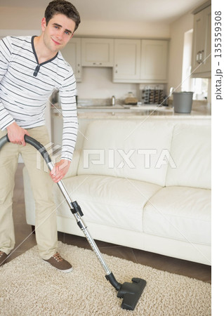 Man vacuuming beige carpet in living room using vacuum cleaner near kitchen countertop, copy space Man vacuuming beige carpet in living room using vacuum cleaner near kitchen countertop, copy space 135359308