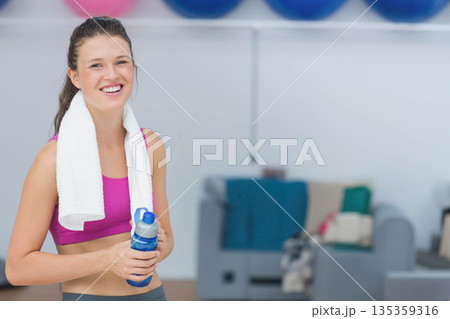 Adult woman in sportswear standing in gym holding water bottle by exercise balls, copy space 135359316