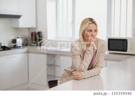 Woman in casual wear biting nails while leaning on white kitchen island, with papers, copy space Woman in casual wear biting nails while leaning on white kitchen island, with papers, copy space 135359340
