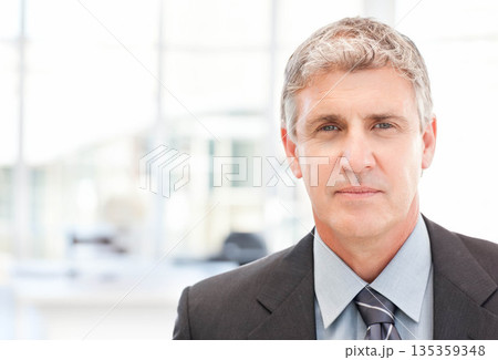 Middle-aged male standing in modern office wearing suit and tie near desks and monitors, copy space 135359348