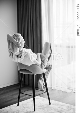 Back view of gorgeous woman relaxing on bar stool. Pretty female sitting on stool with her legs crossed. Woman in blue shirt and jeans looking in window. Black and white image. 135359415