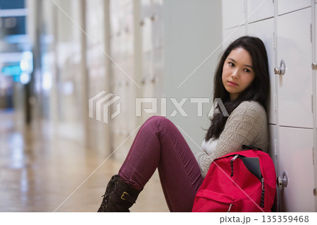 Asian female student sitting on wooden floor in school hallway holding red backpack, copy space Asian female student sitting on wooden floor in school hallway holding red backpack, copy space 135359468