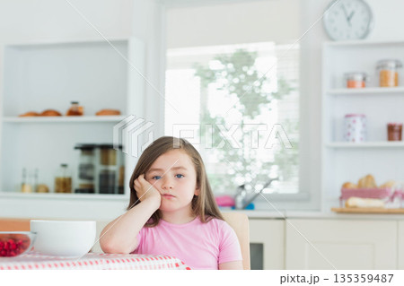 Child girl resting cheek on hand and gazing at kitchen table with berry bowls, checkered tablecloth Child girl resting cheek on hand and gazing at kitchen table with berry bowls, checkered tablecloth 135359487