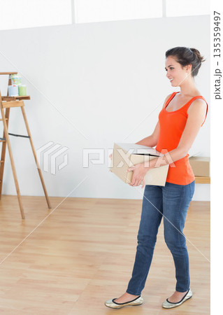Woman holding cardboard box while standing in bright art studio with wooden easel, copy space 135359497