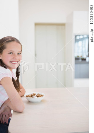 Female child sitting at wooden kitchen counter leaning on arms with cereal bowl spoon, copy space 135359498