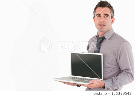 Male in grey shirt and tie standing against white studio backdrop holding silver laptop, copy space Male in grey shirt and tie standing against white studio backdrop holding silver laptop, copy space 135359542