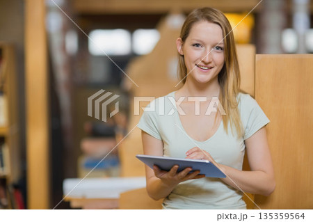 Woman studying in library tapping tablet screen by wooden study carrels and bookshelves, copy space Woman studying in library tapping tablet screen by wooden study carrels and bookshelves, copy space 135359564