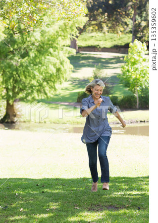 Woman running across grass in sunny park near pond wearing sunglasses on head and slip-on shoes Woman running across grass in sunny park near pond wearing sunglasses on head and slip-on shoes 135359602