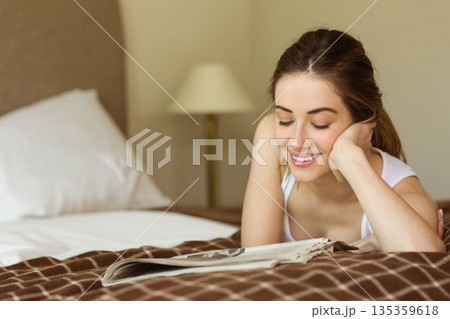 Woman in mid-20s lying on checkered blanket reading magazine in bedroom, copy space Woman in mid-20s lying on checkered blanket reading magazine in bedroom, copy space 135359618