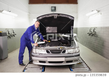 Male technician leaning over sedan engine in garage checking dipstick under hood, copy space Male technician leaning over sedan engine in garage checking dipstick under hood, copy space 135359639