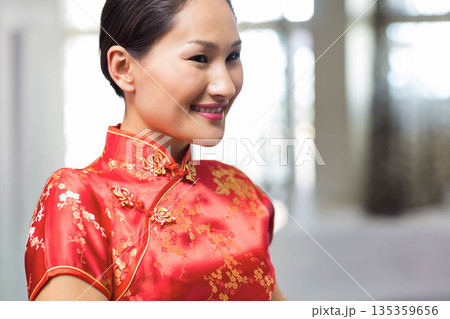 Asian woman smiling in bright lobby wearing red silk cheongsam with gold embroidery, copy space Asian woman smiling in bright lobby wearing red silk cheongsam with gold embroidery, copy space 135359656