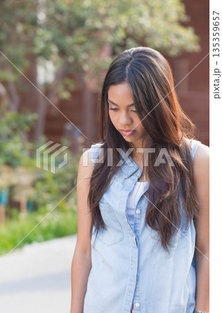 Asian woman standing on paved garden path wearing denim shirt and looking down at green shrubs Asian woman standing on paved garden path wearing denim shirt and looking down at green shrubs 135359657
