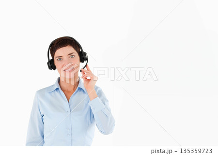 Mid-adult woman standing against seamless white backdrop wearing light blue shirt and headset Mid-adult woman standing against seamless white backdrop wearing light blue shirt and headset 135359723
