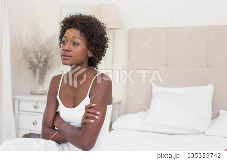 African American woman sitting on bed in bedroom beside nightstand with lamp and vase, copy space 135359742
