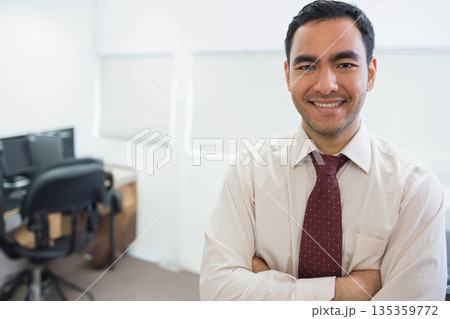 Asian man smiling, crossing arms in office wearing necktie at desk with dual monitors, copy space 135359772