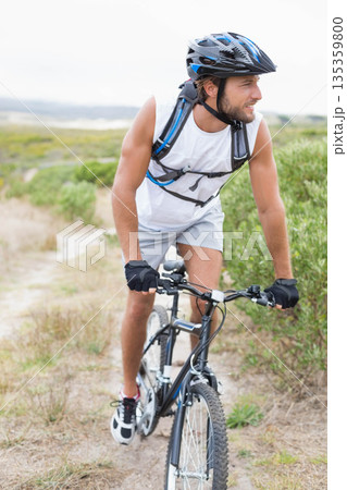 Male cyclist wearing helmet and hydration pack traversing coastal sandy trail on mountain bike 135359800