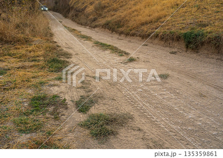 A photograph of deserted dirt road running between the slopes of a mountain gorge, with a car with headlights on emerging from far end. An abstract symbol of a trail leading off in unknown direction A photograph of deserted dirt road running between the slopes of a mountain gorge, with a car with headlights on emerging from far end. An abstract symbol of a trail leading off in unknown direction 135359861