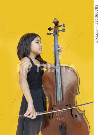 Passionate little Asian girl in black dress playing cello and shouting with joy. Concept for music education, child prodigy, emotional performance, and creative talent Passionate little Asian girl in black dress playing cello and shouting with joy. Concept for music education, child prodigy, emotional performance, and creative talent 135360293