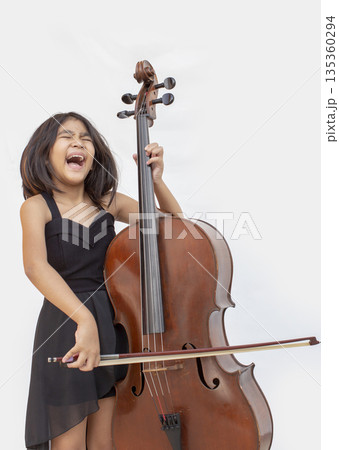 Passionate little Asian girl in black dress playing cello and shouting with joy. Concept for music education, child prodigy, emotional performance, and creative talent 135360294
