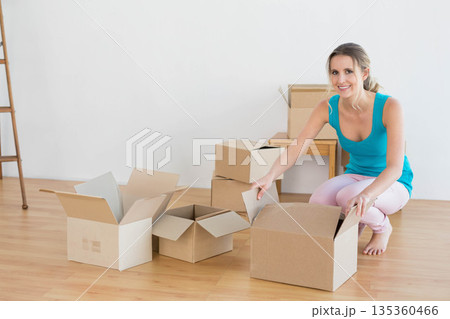 Woman kneeling unboxing cardboard boxes inside new home with ladder and desk, copy space Woman kneeling unboxing cardboard boxes inside new home with ladder and desk, copy space 135360466