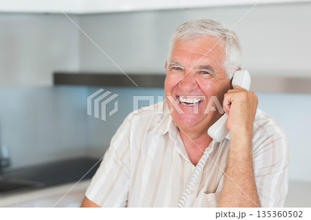 Senior man talking on corded telephone in modern kitchen with countertop and cabinets, copy space Senior man talking on corded telephone in modern kitchen with countertop and cabinets, copy space 135360502