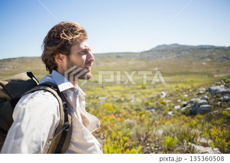 Man in his twenties standing on grassy plateau and carrying hiking backpack, copy space 135360508