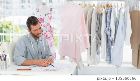 Hispanic man sketching fashion designs with pencil at studio with sewing machine and dress form 135360566