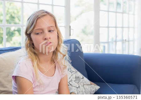 Girl sitting on blue sofa at home leaning on cushion gazing at glass-pane windows, copy space 135360571