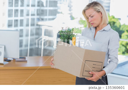 Female office worker packing plant and files into cardboard box beside desk at office, copy space 135360601