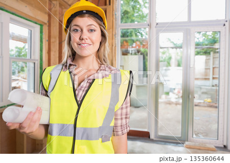 Woman wearing hard hat and vest, holding blueprints and reviewing plans inside renovation site Woman wearing hard hat and vest, holding blueprints and reviewing plans inside renovation site 135360644