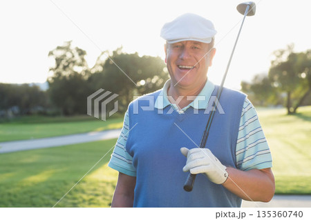 Man wearing polo standing on fairway near paved cart path holding driver over shoulder, copy space 135360740