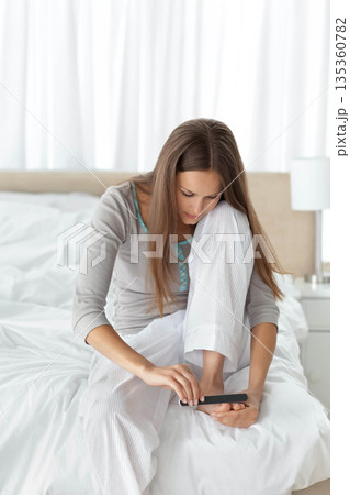 Female sitting on bed with white sheets filing toenails with dark emery board beside white lamp Female sitting on bed with white sheets filing toenails with dark emery board beside white lamp 135360782