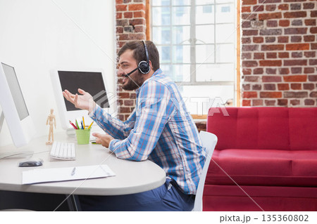 African American man gesturing while speaking in office at desk with dual monitors and headset 135360802