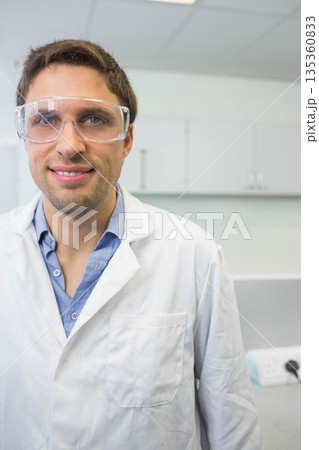 Mid adult male technician standing at bench wearing safety goggles, lab coat in lab, copy space 135360833