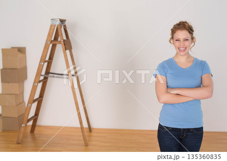 Woman standing near wooden ladder and cardboard moving boxes in empty room, copy space Woman standing near wooden ladder and cardboard moving boxes in empty room, copy space 135360835