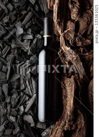 Bottle of red wine against a backdrop of charcoal and dry snags. Bottle of red wine against a backdrop of charcoal and dry snags. 135361025