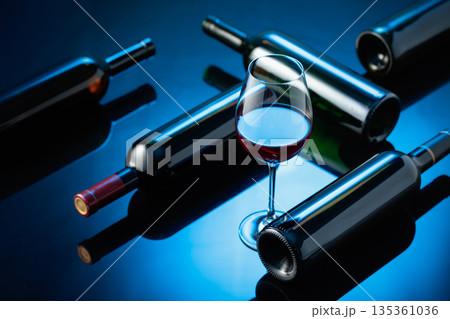 Glass and bottles of red wine on a black reflective background. Glass and bottles of red wine on a black reflective background. 135361036
