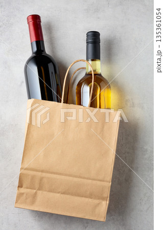 Bottles of red and white wine in a paper bag on a white marble background. 135361054