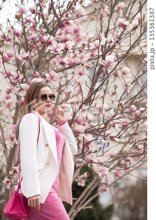 Magnolia flowers woman: Stylish girl poses near blooming magnolia tree, outdoors during spring season. 135361387