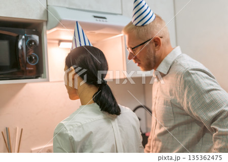 Here's a title following your specifications: **Couple Birthday Party Kitchen Microwave Celebration: Man and woman wearing party hats prepare food in office kitchen during birthday celebration.** 135362475