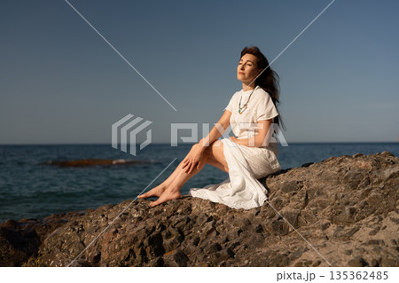Woman beach relaxation, peaceful adult female enjoys sun on rocky shore with ocean horizon, summer vacation, copy space. Woman beach relaxation, peaceful adult female enjoys sun on rocky shore with ocean horizon, summer vacation, copy space. 135362485