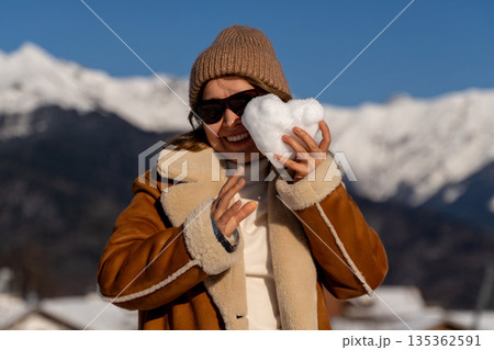 Snow Heart Woman Alps Winter: Joyful snow heart held by woman, sunny Alps mountains backdrop, winter season. 135362591