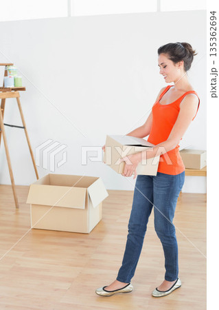 Woman holding cardboard box and standing by easel with paint cans in bright room, copy space 135362694