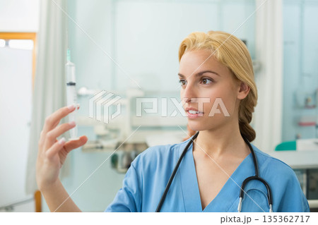 Female medical professional examining green fluid syringe in exam room with stethoscope, copy space 135362717
