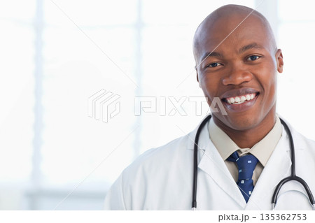 African American male doctor wearing lab coat, holding stethoscope by clinic windows, copy space 135362753