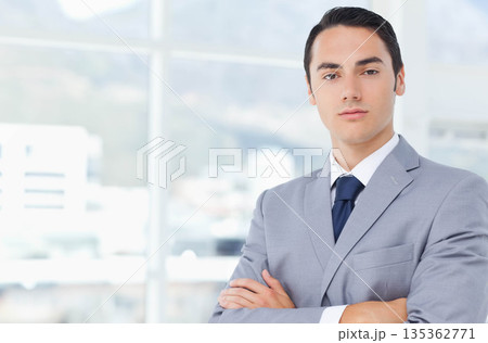 Man in early thirties wearing grey suit standing in office near tall glass windows, copy space Man in early thirties wearing grey suit standing in office near tall glass windows, copy space 135362771