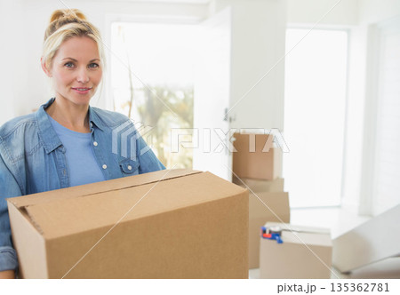 Woman holding cardboard box in entryway with moving boxes by open front door, copy space 135362781