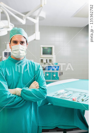 Male surgeon in scrubs standing beside table in operating room with instrument tray, copy space Male surgeon in scrubs standing beside table in operating room with instrument tray, copy space 135362782